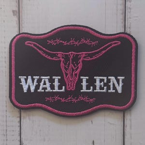 May include: A rectangular embroidered patch with rounded corners featuring a black background and a pink border. The design includes a pink steer skull graphic, pink barbed wire accents, and the white text WAL LEN centered on the patch.