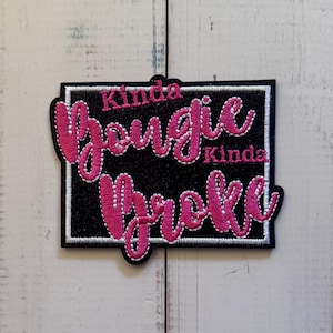 May include: A rectangular embroidered patch with a black glitter background and a white stitched border. The text Kinda Bougie Kinda Broke is embroidered in bright pink cursive lettering, with the words Kinda positioned above and below.