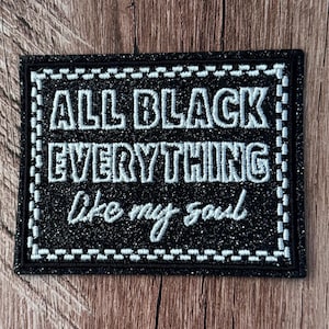 May include: A rectangular black glittery embroidered patch featuring the white stitched text ALL BLACK EVERYTHING and the cursive script like my soul. The patch has a white stitched border with a checkered pattern and a black outer edge.