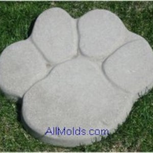 Puede incluir: Un adoquín de huella de pata de animal de hormigón gris con cinco dedos. El adoquín está sobre un lecho de hierba verde.