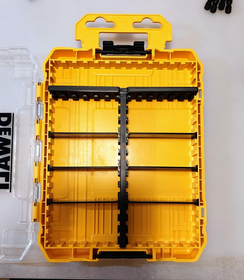 May include: Yellow and black tool organizer with a clear plastic lid. The organizer has multiple compartments and a handle for easy carrying. The brand name "DEWALT" is visible on the clear lid. The interior is divided into sections for storing tools.