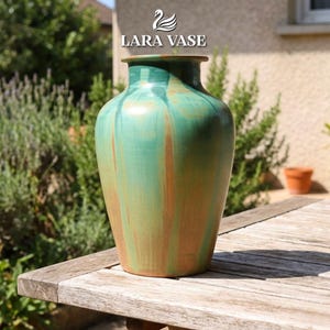 Könnte beinhalten: Eine große, handgefertigte Vase mit breitem Boden und schmalem Hals. Die Vase weist eine Mischung aus grünen und braunen Farbtönen auf, die eine einzigartige, erdige Ästhetik erzeugt. Der Text "LARA VASE" wird oben angezeigt. Die Vase steht auf einem Holztisch.