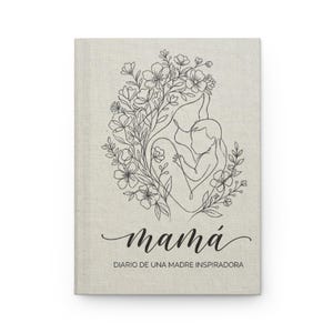 Puede incluir: Un diario con una cubierta de lino que presenta un dibujo lineal negro de una madre y un niño rodeados de flores. La palabra "mamá" está escrita en cursiva, con "DIARIO DE UNA MADRE INSPIRADORA" debajo.