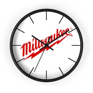 Könnte beinhalten: Eine runde Wanduhr mit schwarzem Rahmen und weißem Zifferblatt. In der Mitte befindet sich das rote Milwaukee-Logo mit einer Blitzgrafik. Die Uhr hat schwarze Stunden-, Minuten- und Sekundenzeiger sowie einfache schwarze Strichmarkierungen.