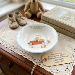 May include: Vintage Shelley bowl, "Fairies Love Motoring" by Mabel Lucie Attwell. The white bowl features a light blue rim and a charming illustration of a red car with children and fairies. The bowl is 5.25 inches in diameter.