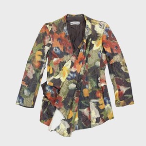 Puede incluir: Un blazer con estampado floral y frente drapeado. La chaqueta presenta un cuello en V y mangas largas. El patrón incluye flores rojas, naranjas, amarillas, azules y verdes sobre un fondo oscuro. La marca es visible.