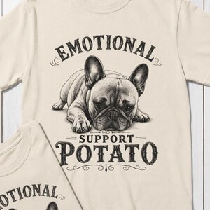 May include: Two cream-colored t-shirts with a graphic of a French Bulldog. The shirts have the text "EMOTIONAL" above the dog and "SUPPORT POTATO" below. The dog illustration is in black and white.