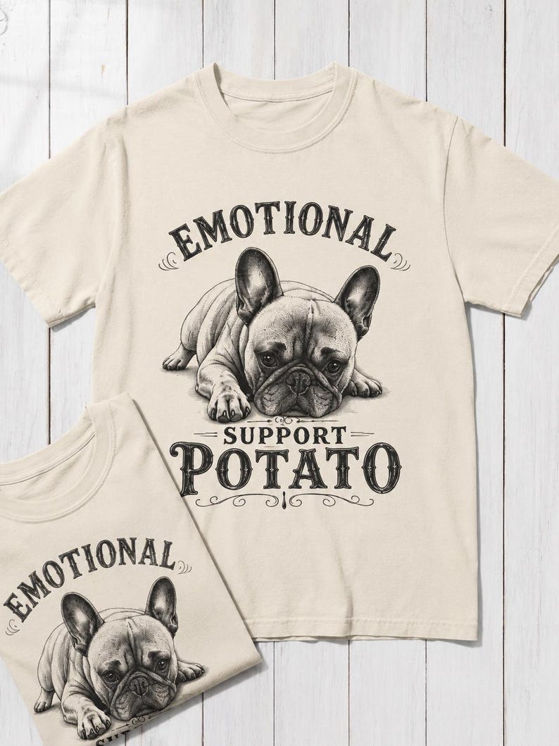 May include: Two cream-colored t-shirts with a graphic of a French Bulldog. The shirts have the text "EMOTIONAL" above the dog and "SUPPORT POTATO" below. The dog illustration is in black and white.