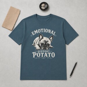 Może przedstawiać: Granatowa koszulka z grafiką przedstawiającą buldoga francuskiego i napisem "EMOTIONAL SUPPORT POTATO". Pies jest przedstawiony w pozycji leżącej. Tekst i grafika psa są białe. Koszulka jest wykonana z miękkiego materiału.