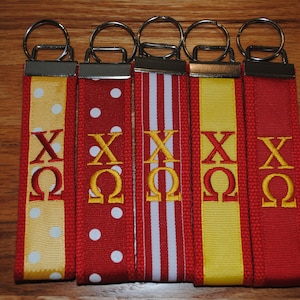 May include: Five red, white, and yellow keychains with gold embroidery of the letters "XO" and the Greek letter "Omega".