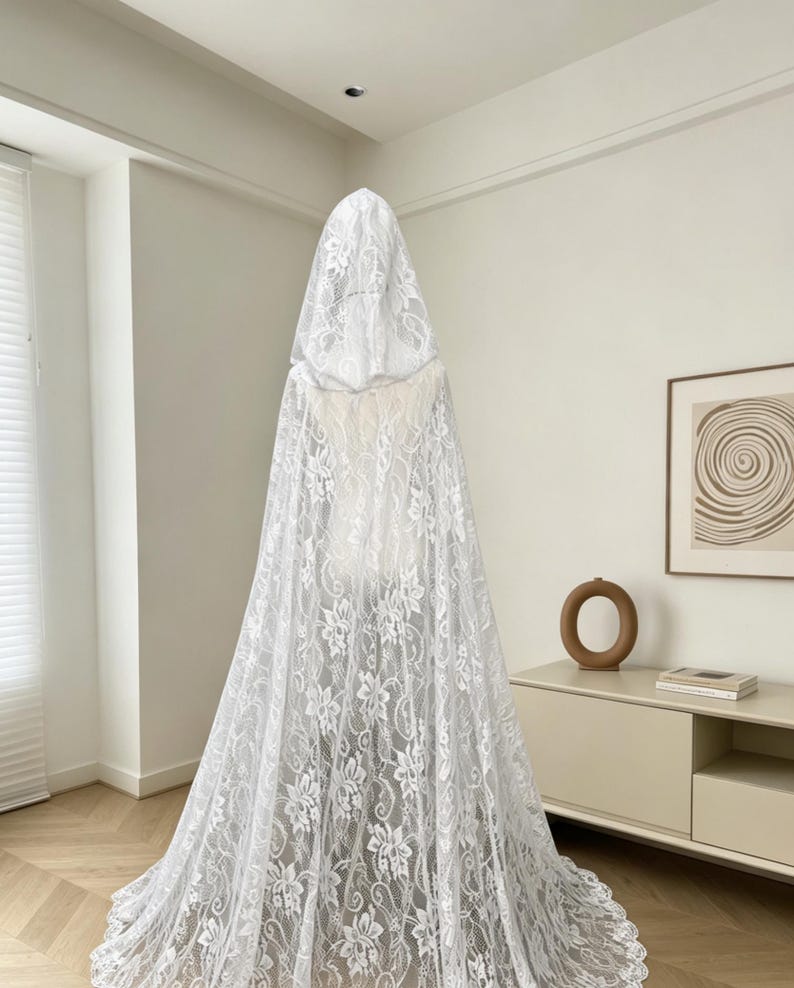May include: A white lace hooded cape, displayed on a mannequin. The cape features a floral pattern and a long, flowing design. The hood is also made of the same delicate lace material.
