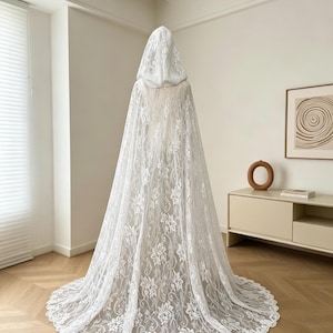 May include: A white lace hooded cape with a floral pattern. The cape is long, flowing, and covers the entire body. The hood is also made of lace and is attached to the cape. The cape is designed to be worn over clothing.