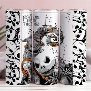 May include: A white tumbler featuring characters and imagery from "The Nightmare Before Christmas." The design includes Jack Skellington, Sally, and other characters in a black and white color scheme, with orange accents. The text "The Nightmare Before Christmas" is also visible.