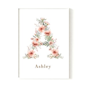Könnte beinhalten: Gerahmter Druck mit dem Buchstaben "A", gebildet aus pfirsichfarbenen Blumen und grünen Blättern. Der Name "Ashley" ist in Braun unter dem floralen Buchstaben auf weißem Hintergrund gedruckt.