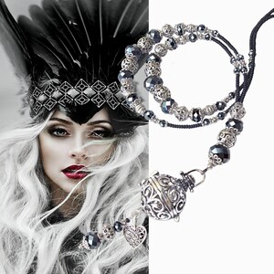 May include: A black and silver beaded necklace with a silver charm pendant. The charm is a cage-like design with a heart hanging from it. The necklace is on a white background.