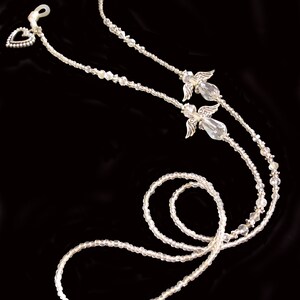 May include: A pair of clear crystal angel wing eyeglass holders with silver accents. The holders are connected by a beaded chain with a heart charm.