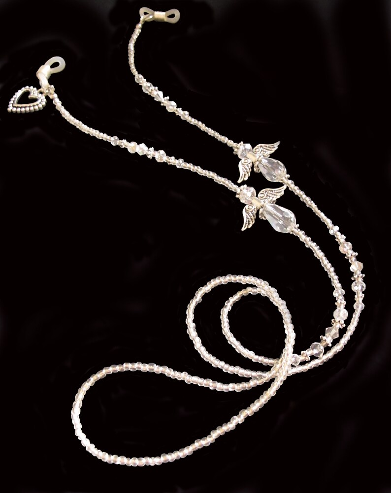 May include: A pair of clear crystal angel wing eyeglass holders with silver accents. The holders are connected by a beaded chain with a heart charm.