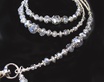 May include: A silver beaded lanyard with a face charm. The lanyard is made of small silver beads and has a silver clasp. The face charm is a silver pendant with a detailed face design.