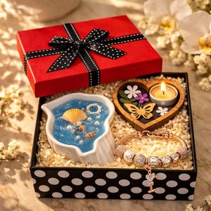 May include: A gift set in a black polka dot box with a red lid and black ribbon. Inside, a blue seashell-themed candle, a wooden heart-shaped candle holder with a lit candle, and a charm bracelet are displayed.