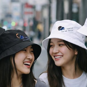 May include: Four people wearing black and white bucket hats. Each hat has the text "Internet Server Error" and a graphic embroidered on it. The hats are black and white. The people are smiling in a city setting.