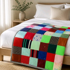 May include: A vibrant patchwork quilt featuring squares of various fabrics in shades of red, blue, green, and brown. The quilt is draped over a white bed, complemented by a neutral pillow and a wooden bed frame. The quilt's border is a solid grey.