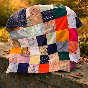 Pode incluir: Uma colcha de retalhos feita à mão com quadrados de tecido variados em tons de azul, verde, laranja, amarelo e rosa. A colcha está drapeada sobre uma superfície de pedra, mostrando suas cores e texturas vibrantes. Um item decorativo e aconchegante.