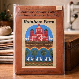 May include: A machine appliqué pattern and instructions titled "Rainbow Farm." The cover features a red barn with a blue sky, a rainbow, and white ducks. Finished size is approximately 11" x 19".