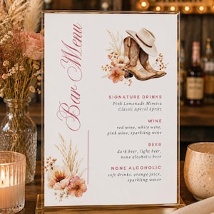 May include: A vertical rectangular bar menu sign in a gold frame featuring the text Bar Menu, Signature Drinks, Wine, Beer, and None Alcoholic. The design includes watercolor illustrations of a cowboy hat, brown boots, and dried floral arrangements.
