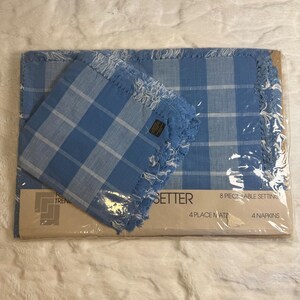 May include: An 8-piece table setting set in clear plastic packaging, containing 4 placemats and 4 napkins. The fabric features a blue and white checkered pattern with frayed edges. The label reads 8 PIECE TABLE SETTING, 4 PLACE MATS, 4 NAPKINS.