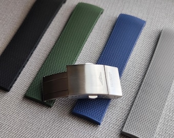 May include: A collection of watch straps in black, green, blue, and gray, with a silver-tone buckle. The straps have a textured surface and are arranged on a neutral background. The buckle is engraved with the brand name.