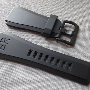 以下が含まれることがあります： バックルとストラップに「BR」の文字がエンボス加工された黒い時計ストラップ。 ストラップには一連の長方形の切り欠きがあります。 バックルも黒です。