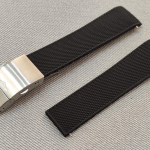 May include: Black watch strap with a textured surface and a silver-colored clasp. The clasp has the brand name "Longines" engraved on it. The strap is made of a durable material and is designed to be water resistant.