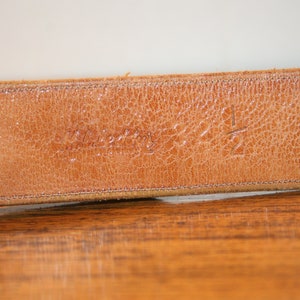 Op de afbeelding: Close-up van een bruine leren riem met de tekst "Westerly" en het nummer "12" gegraveerd op de achterkant.
