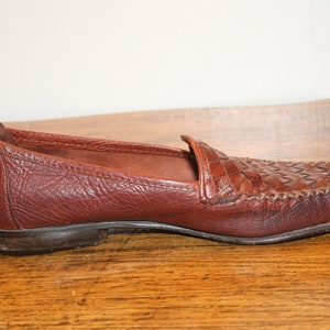 Op de afbeelding: Een paar bruine leren loafers met een geweven patroon op de neus. De loafers hebben een simpel ontwerp en een comfortabele uitstraling.