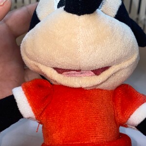 Op de afbeelding: Een pluche speelgoed van Minnie Mouse, die een rode jurk met witte stippen draagt. Ze heeft zwarte ogen, een zwarte neus en een rode strik op haar hoofd.