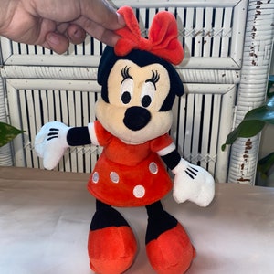 Op de afbeelding: Een rood en zwart pluche speelgoed van Minnie Mouse. Ze draagt een rode jurk met witte stippen en een rode strik.