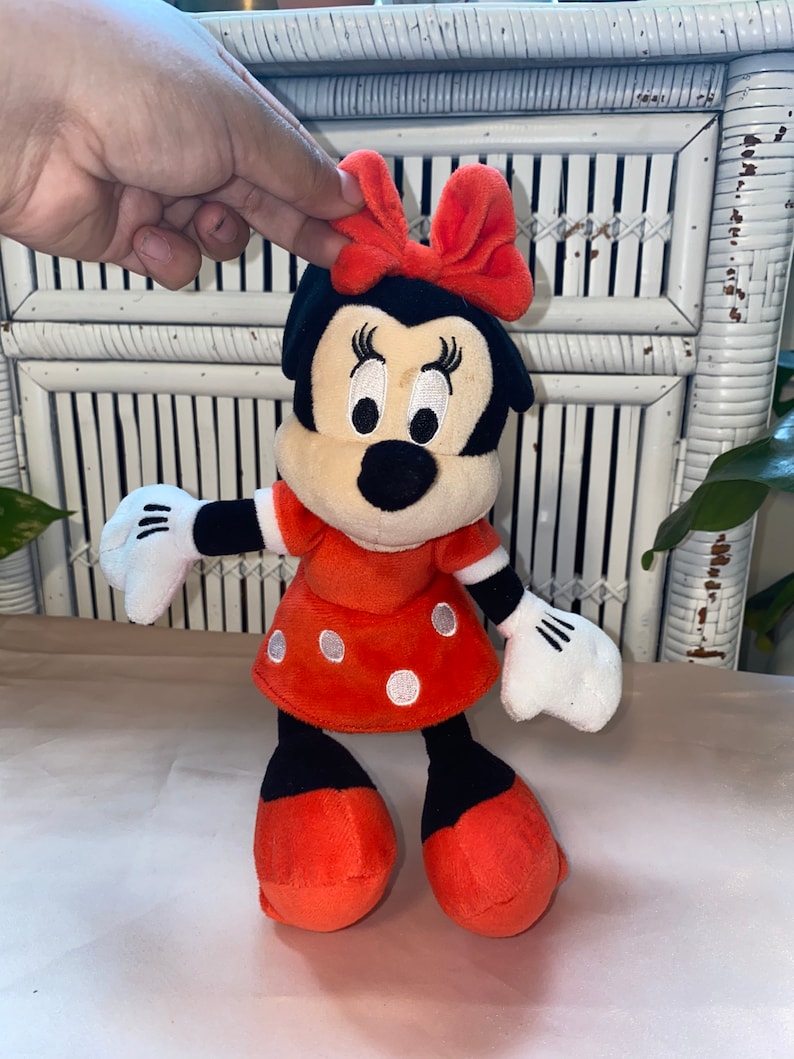 Op de afbeelding: Een rood en zwart pluche speelgoed van Minnie Mouse. Ze draagt een rode jurk met witte stippen en een rode strik.