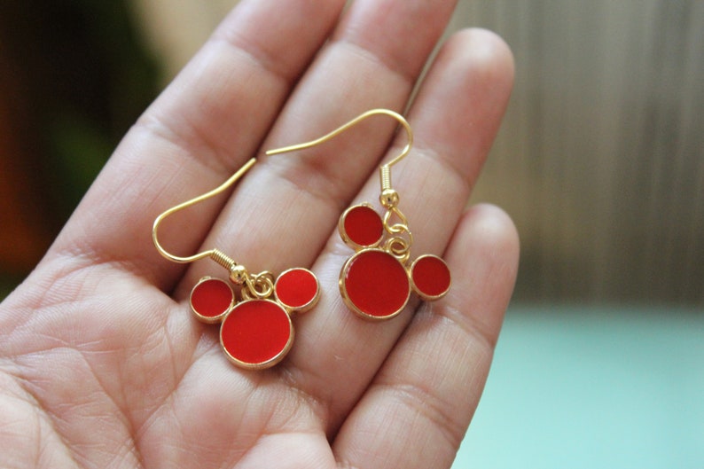 May include: A pair of gold dangle earrings with red enamel Mickey Mouse heads.