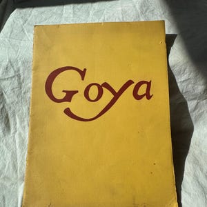 Może przedstawiać: Żółta okładka książki z tytułem "Goya" w bordowym skrypcie. Okładka nosi ślady użytkowania, co wskazuje na starsze wydanie. Książka jest prawdopodobnie biografią.