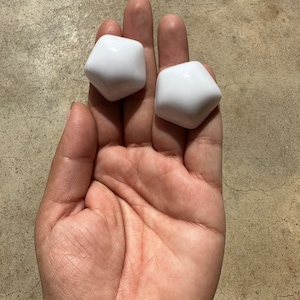 Puede incluir: Dos pomos de cerámica blancos, de forma geométrica y lisos.