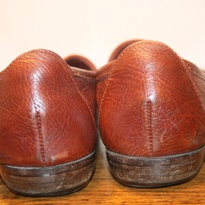 Op de afbeelding: Een paar bruine leren loafers met een licht verweerde uitstraling. De schoenen hebben een afgeronde neus en een lage hak.