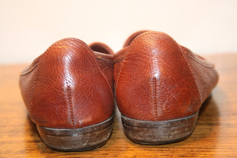 Op de afbeelding: Een paar bruine leren loafers met een licht verweerde uitstraling. De schoenen hebben een afgeronde neus en een lage hak.