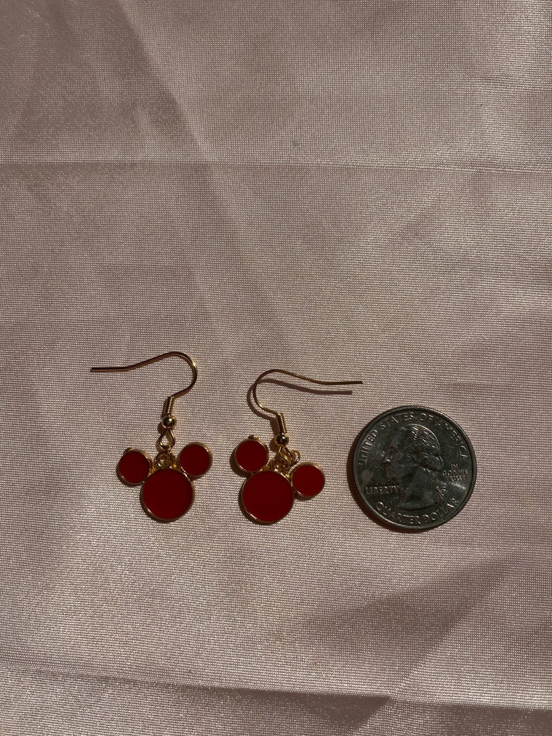 May include: A pair of gold-tone earrings with red Mickey Mouse-shaped charms. The earrings are about the size of a US quarter.