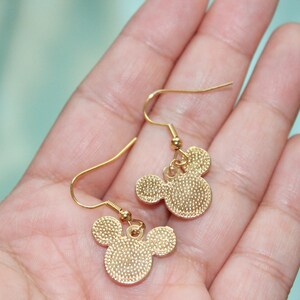 May include: A pair of gold-tone dangle earrings featuring a Mickey Mouse head design. The earrings have a simple hook closure.
