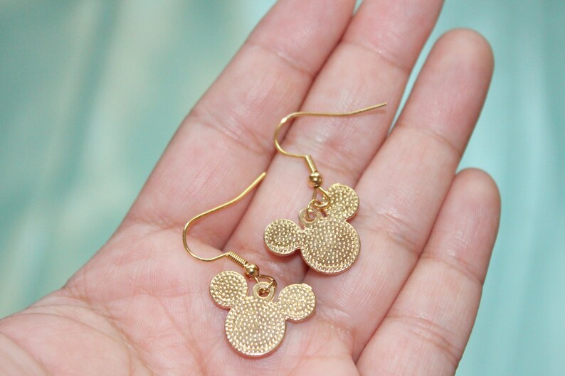 May include: A pair of gold-tone dangle earrings featuring a Mickey Mouse head design. The earrings have a simple hook closure.