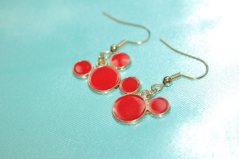 May include: Red and gold Mickey Mouse-shaped earrings. The earrings have three red circles on each side.