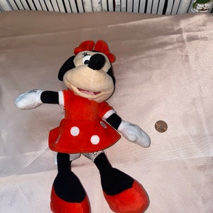 Op de afbeelding: Een rode jurk met witte stippen en een zwarte strik op het hoofd. Het pluche speelgoed is een cartoonfiguur met een zwarte neus en grote ogen.