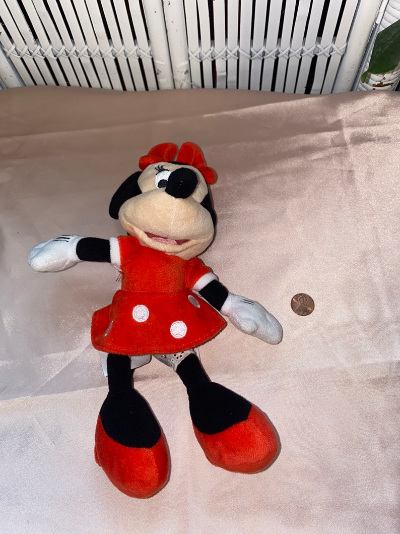 Op de afbeelding: Een rode jurk met witte stippen en een zwarte strik op het hoofd. Het pluche speelgoed is een cartoonfiguur met een zwarte neus en grote ogen.