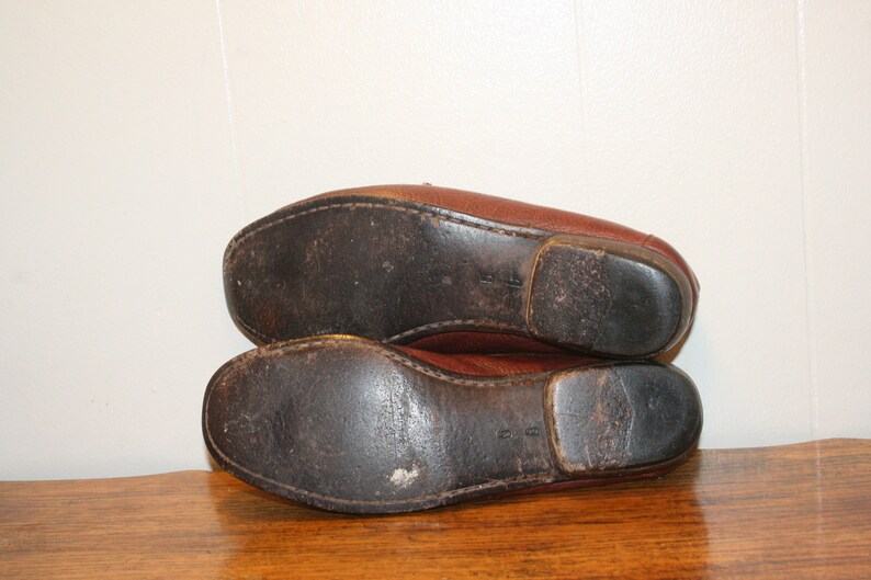 Op de afbeelding: Een paar bruine leren loafers met versleten leren zolen. De loafers liggen op elkaar.