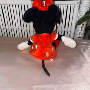 Op de afbeelding: Een rood en zwart pluche speelgoed van Minnie Mouse. Ze draagt een rode jurk met witte stippen en heeft een zwarte staart.